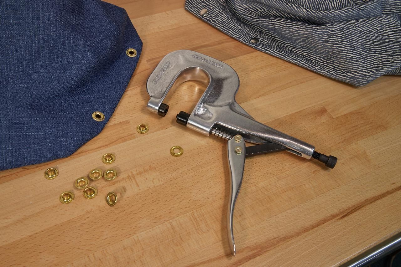 A metal grommet tool on a wooden surface with fabric and grommets.
