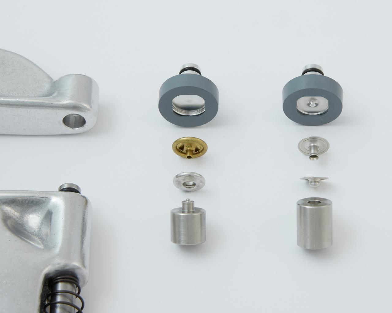Disassembled components of a metallic mechanism, including gray rubber rings, screws, and cylinders, on a white surface.