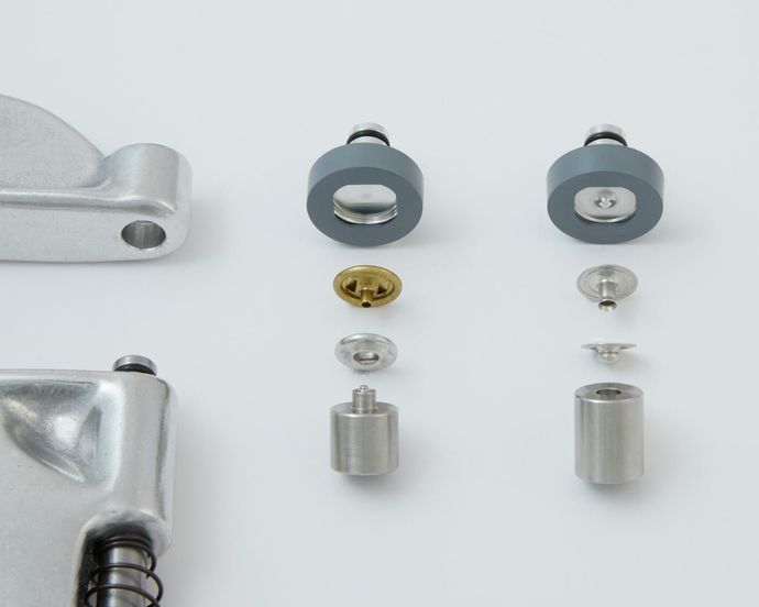 Disassembled components of a metallic mechanism, including gray rubber rings, screws, and cylinders, on a white surface.