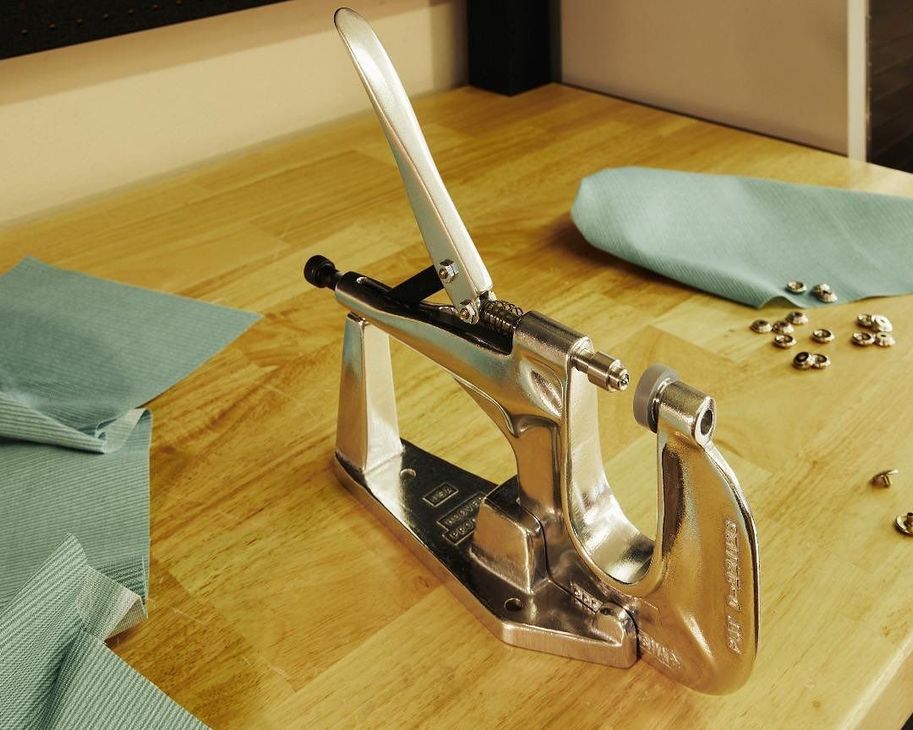 Metal grommet press on a wood surface, with blue fabric and grommets.