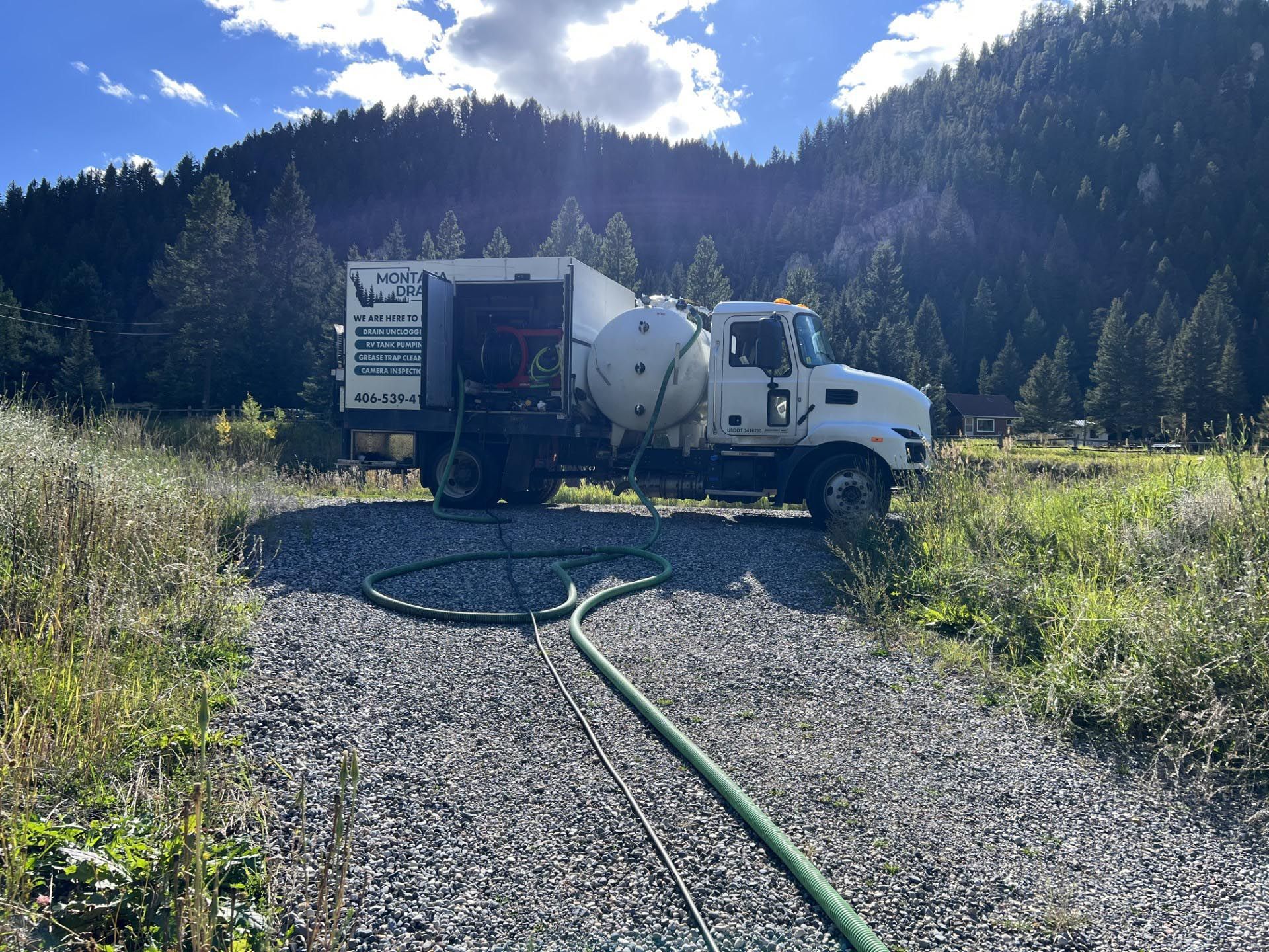 A white truck is parked on a gravel road with a hose attached to it.