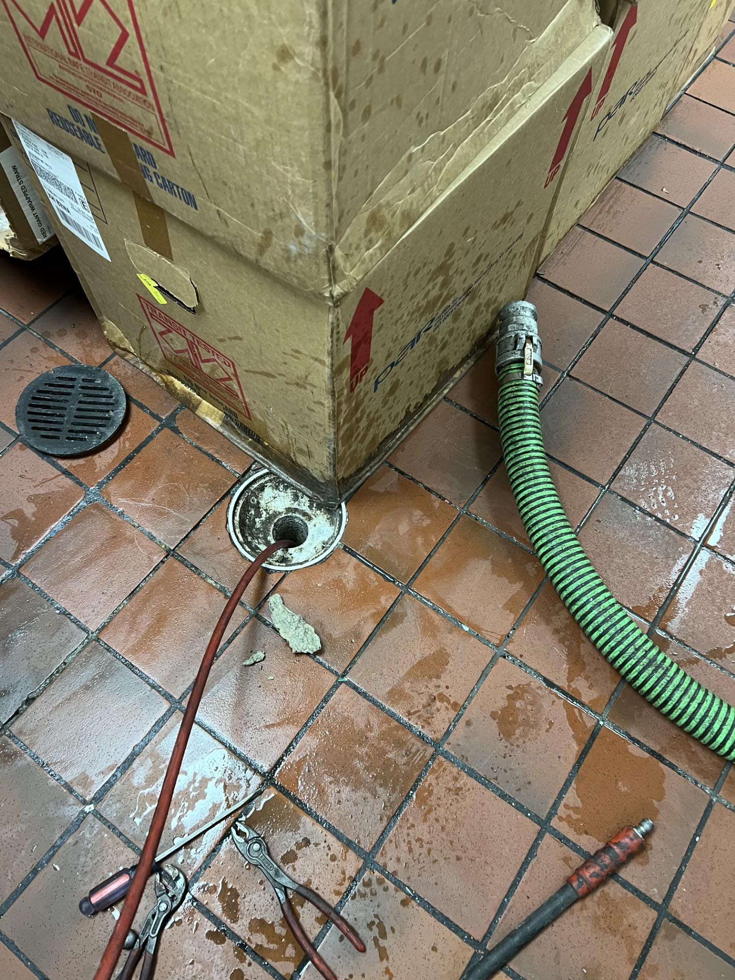 A green hose is connected to a box on a tiled floor.