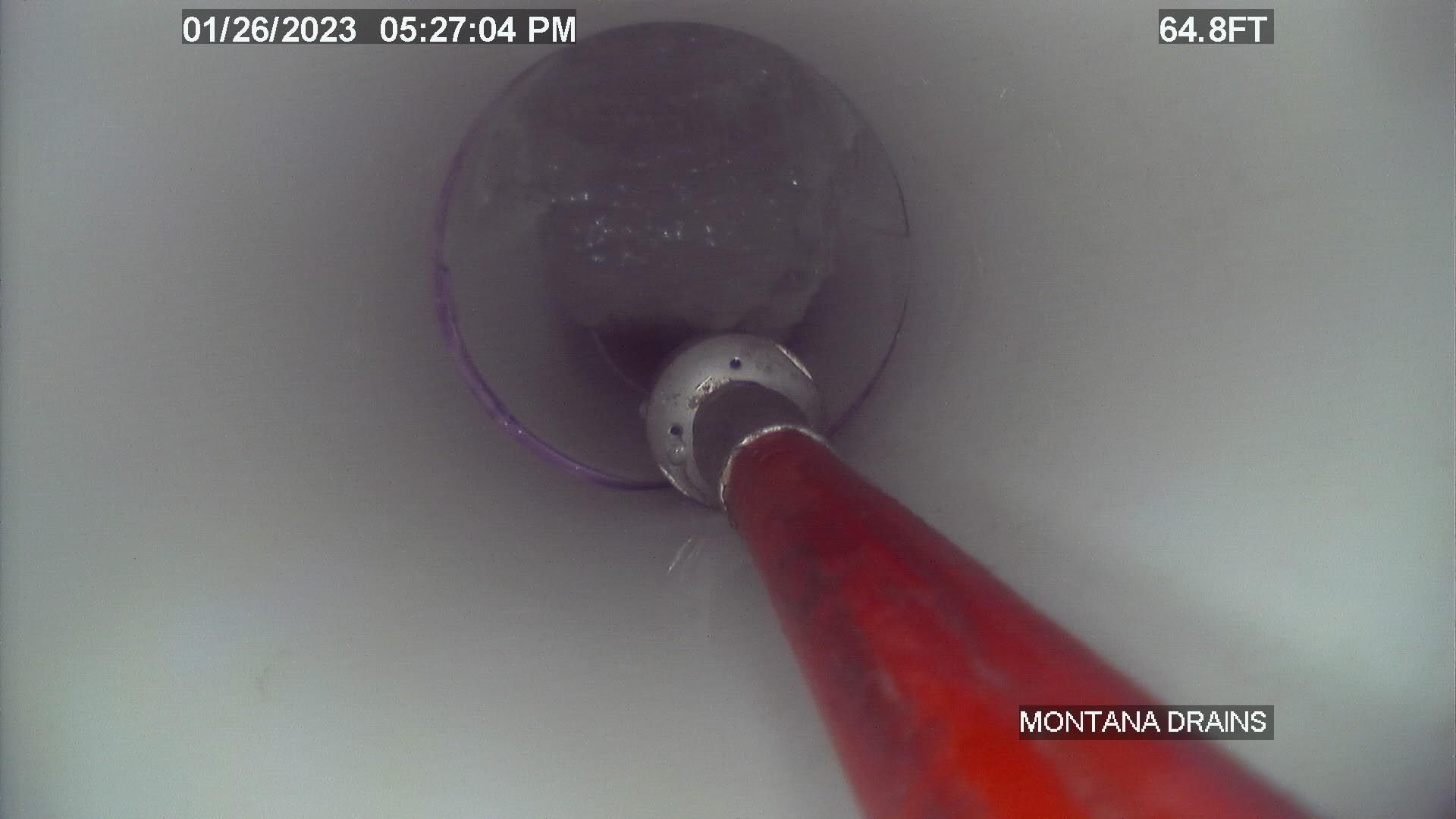 A red hose is being used to clean a pipe.