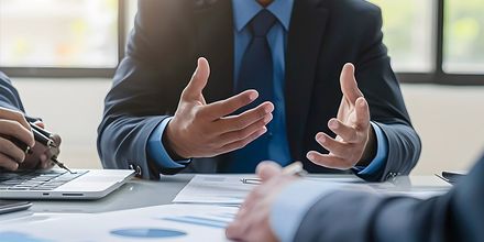 Réunion d’affaires où des personnes en costume discutent autour de documents, à une table de conférence