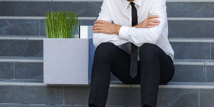 Personne en chemise blanche et cravate noire assise sur des marches en pierre, à côté d’une jardinière avec de l’herbe verte.
