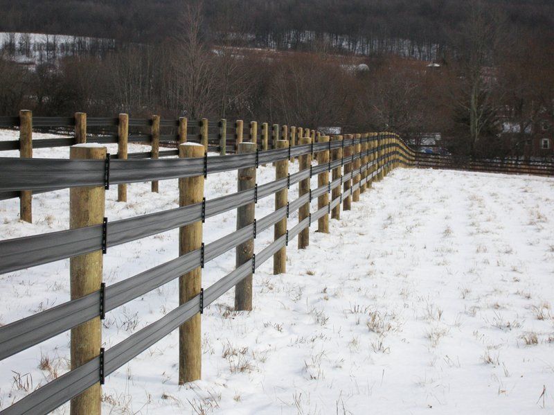 Snowy fence stretching into the distance beside a winter field and trees
