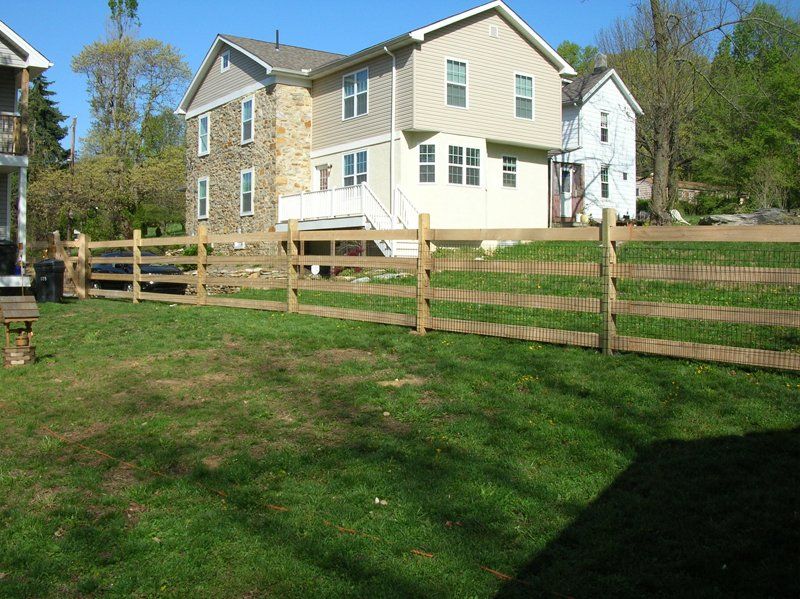 Two-story beige house with a wooden fence and grassy yard on a sunny day
