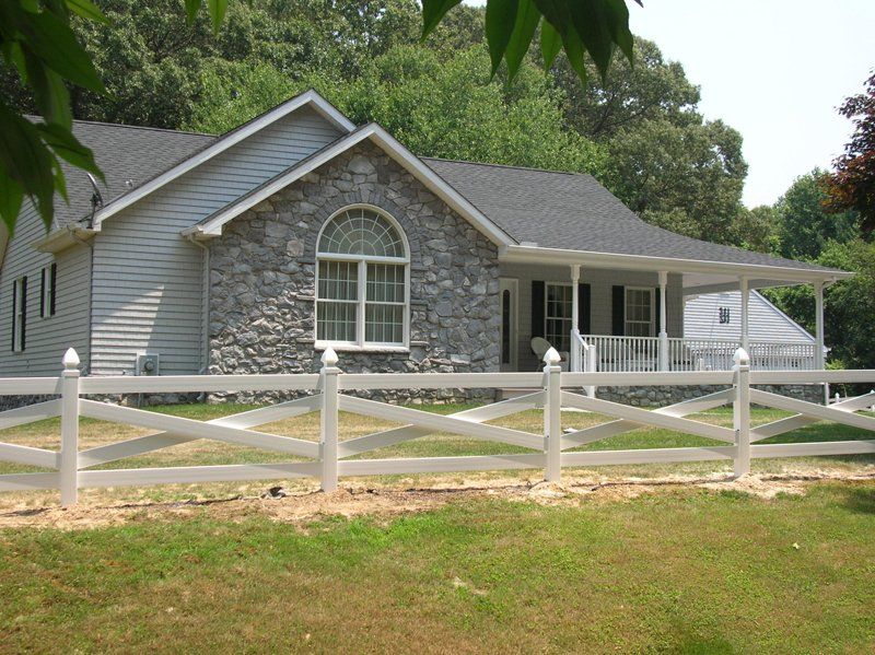 Stone house with white fence and porch, surrounded by green trees and grass.