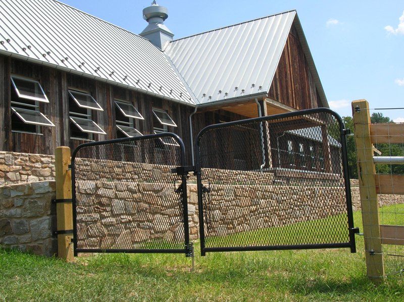 Rustic stone barn with a metal roof behind a wire fence on a grassy lawn