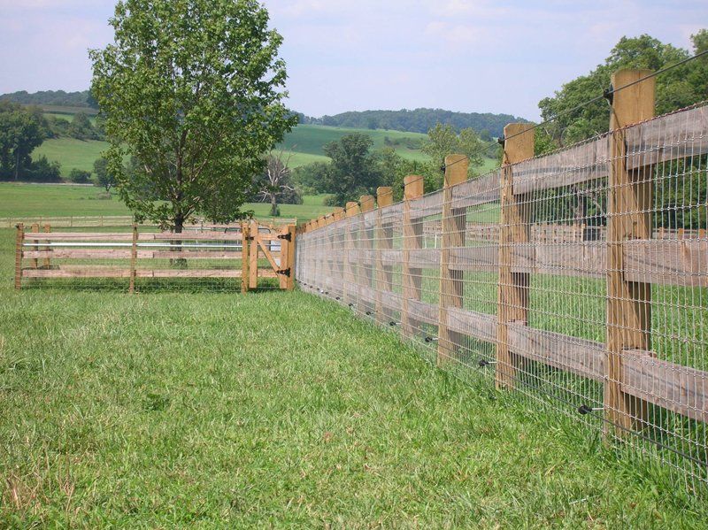Wooden fence along a grassy field with a tree and rolling hills in the background.
