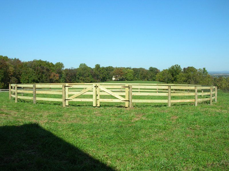 Circular fenced grassy field under a blue sky with trees in the background