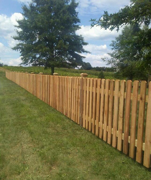 Wooden fence along a grassy yard with trees under a partly cloudy sky