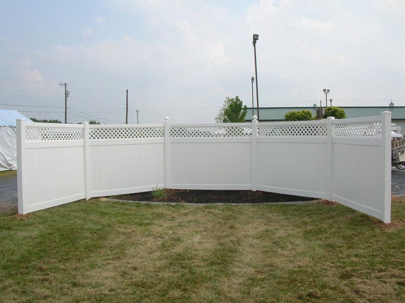 White vinyl fence with an open gate on a grassy yard under a cloudy sky