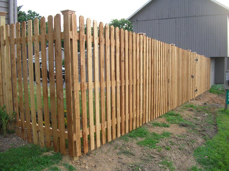 Wooden fence with vertical slats along a grassy yard beside a gray building
