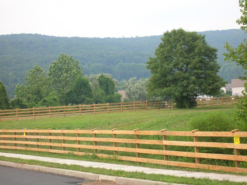 Wooden fence along a grassy field with trees and hills in the background