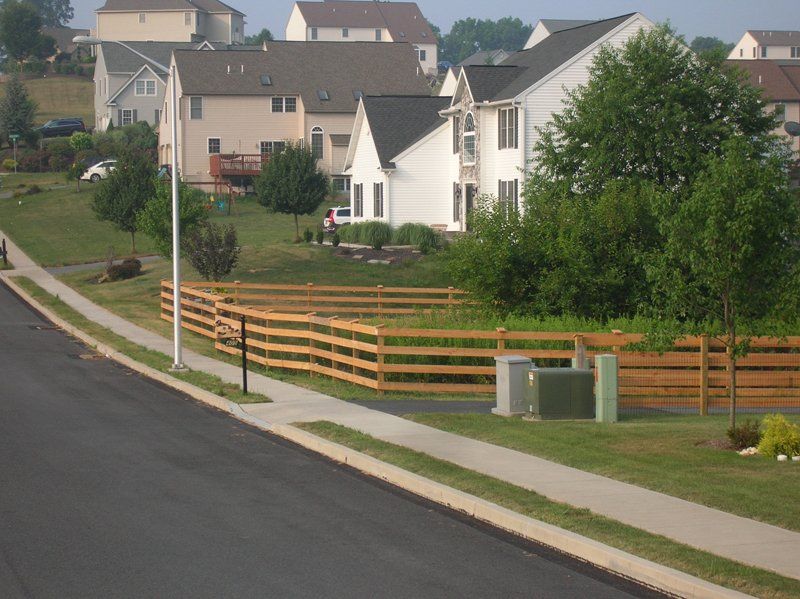 Suburban street with sidewalks, wooden fence, trees, and beige houses on a sunny day