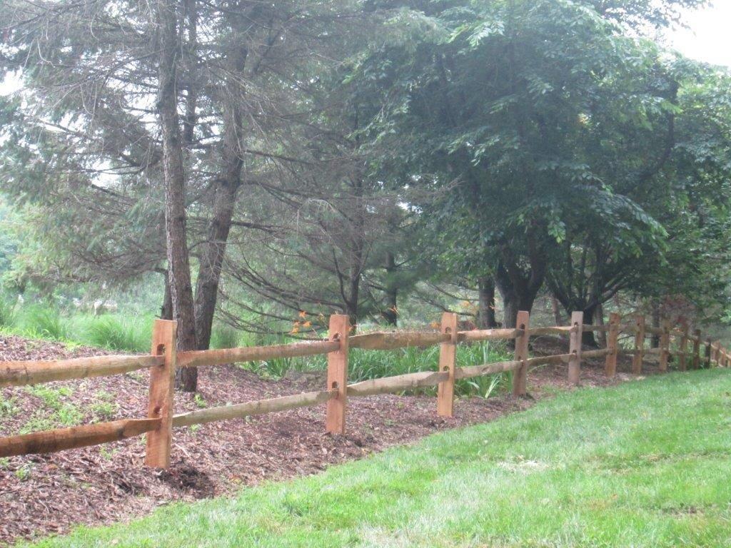 Wooden fence along a grassy path beside trees in a wooded park area.
