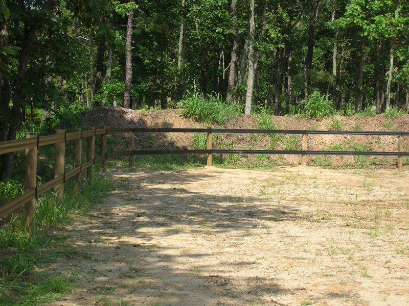 Wooden fence bordering a sunlit sandy path beside a leafy forest