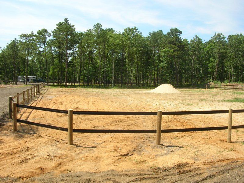Sand riding arena with wooden fence, sandy ground, and trees in the background