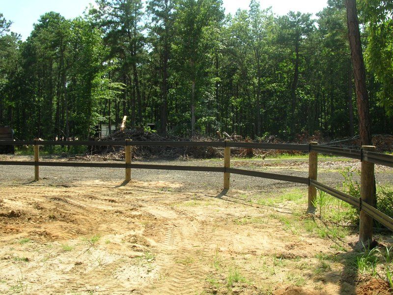 Wooden fence around a sandy clearing beside a forest of green trees