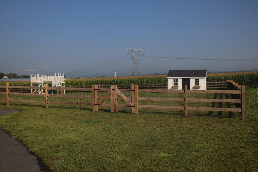 Wooden fence and gate around a grassy field with a small white shed under a clear blue sky.