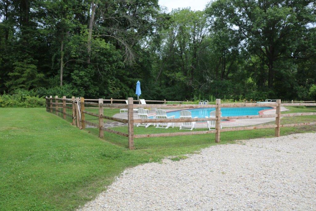 Fenced outdoor swimming pool with blue water beside a gravel path and trees.