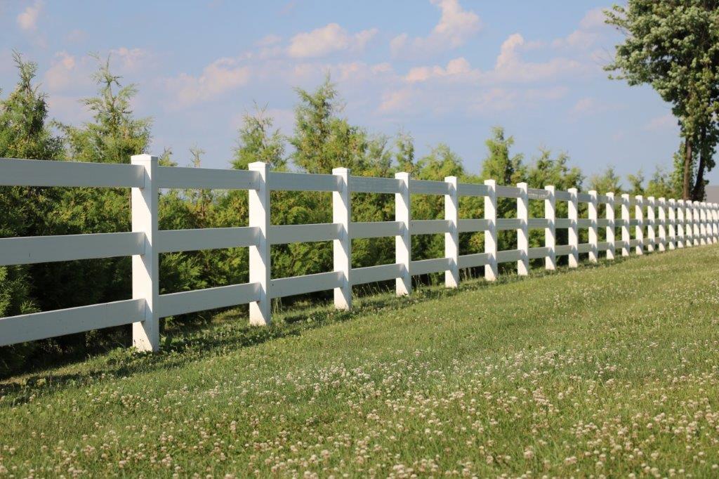White fence running along a grassy hillside under a blue sky with clouds