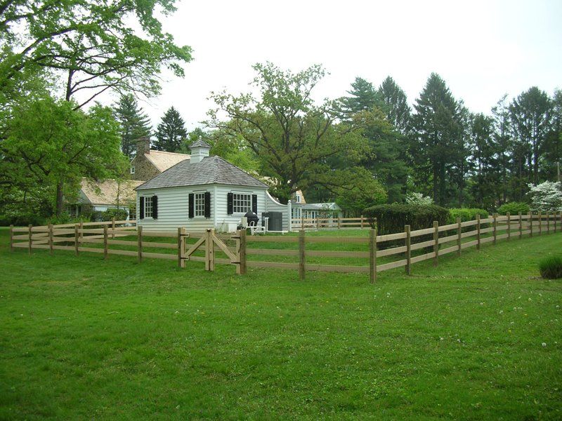 Small white house with a fenced grassy yard and trees under an overcast sky