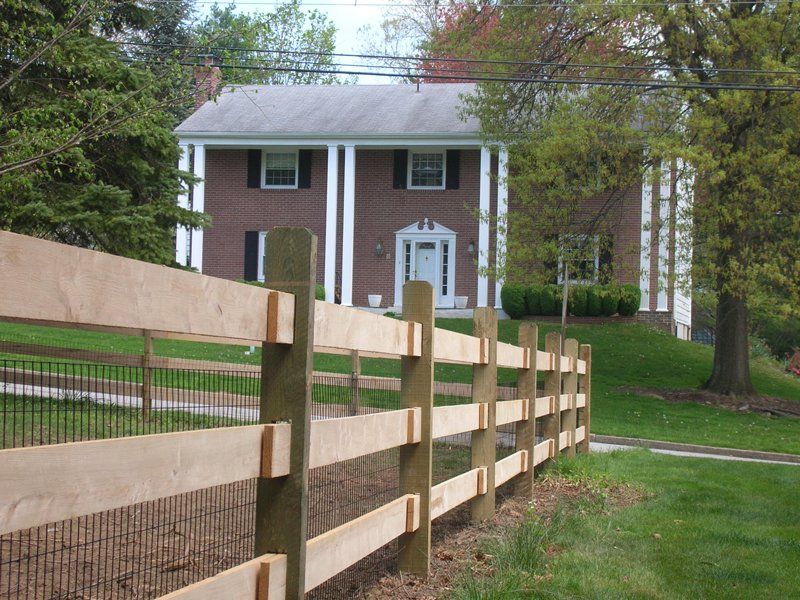 Brick house behind a wooden fence with trees and a grassy yard