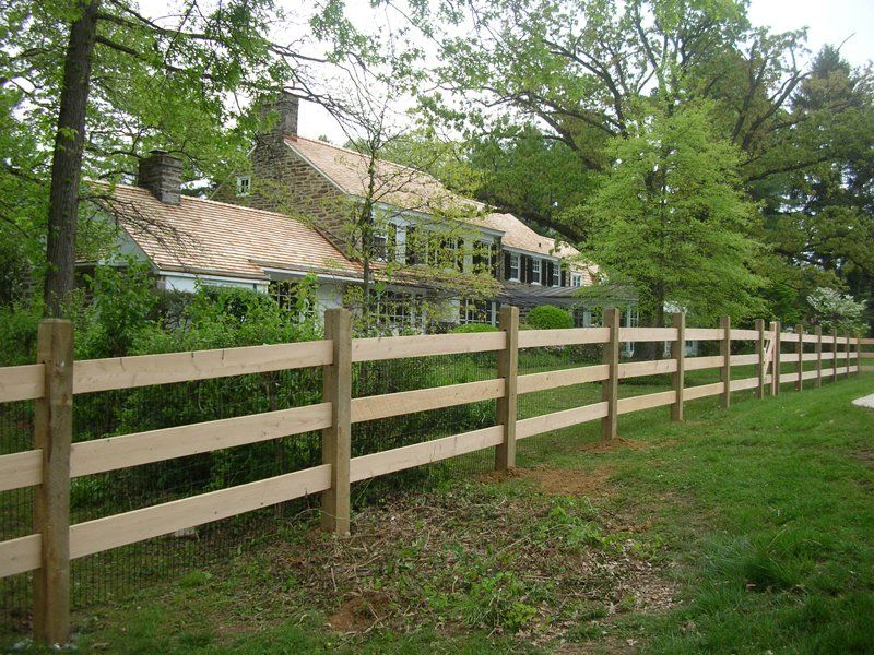 Wooden fence along a grassy yard with trees and a house in the background