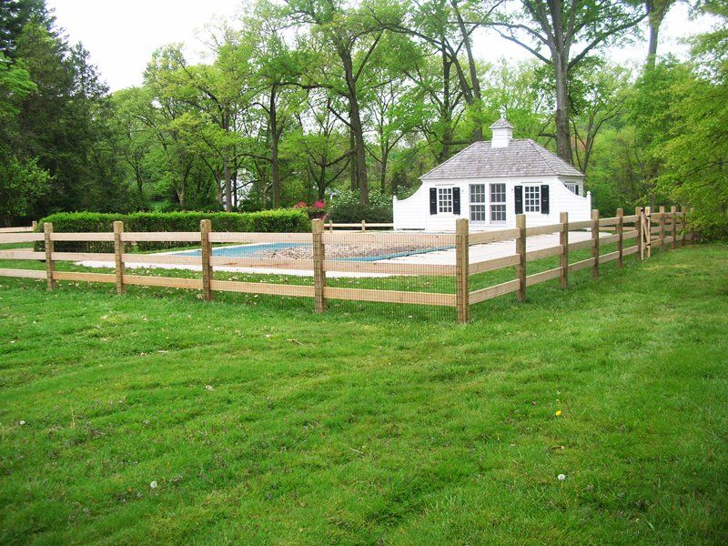 White cottage with a fenced yard surrounded by trees and green grass