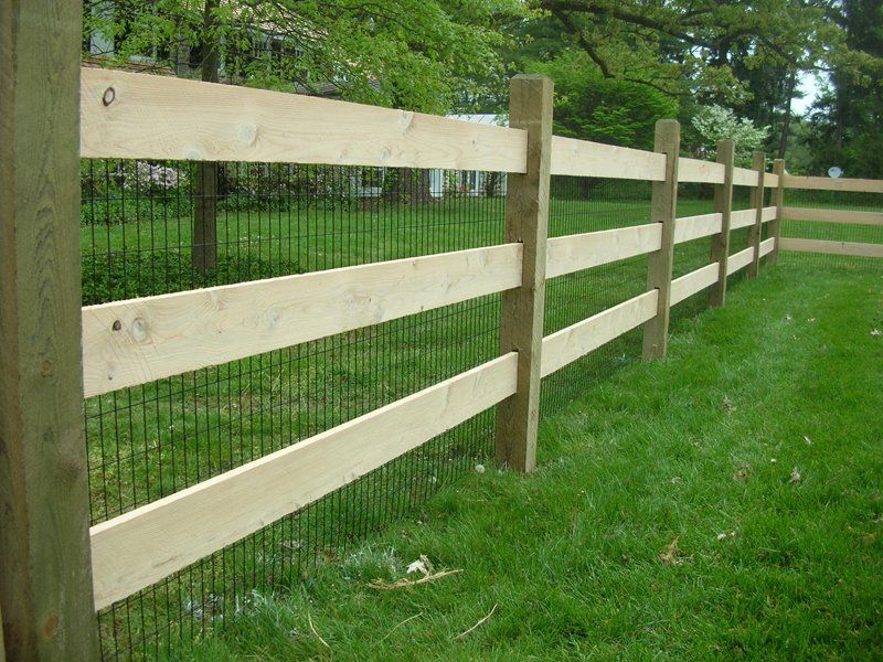 Light wood fence with wire mesh along a grassy yard beside trees