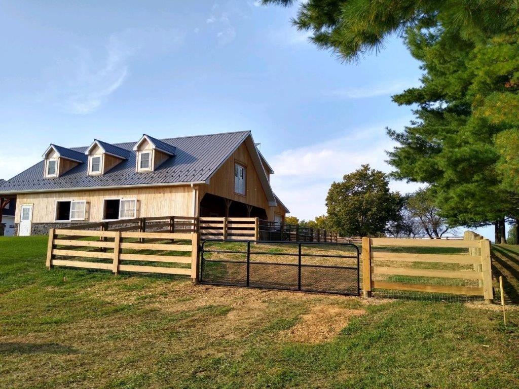 Rural barn and fenced pasture under a blue sky, with a large tree on the right