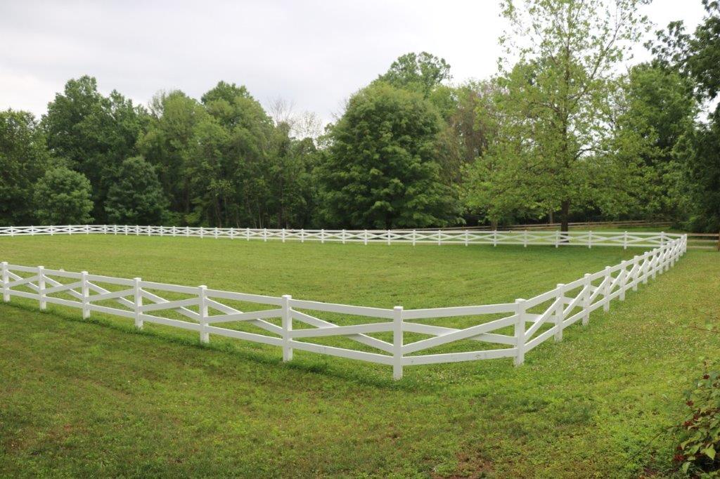 White fenced grassy pasture with trees in the background
