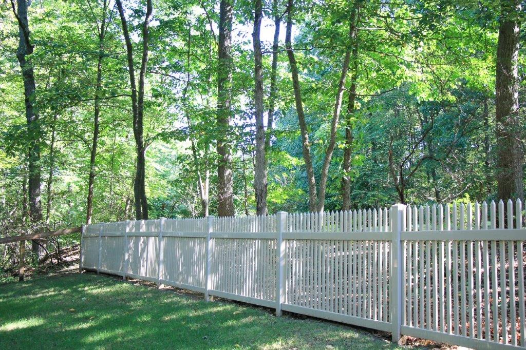 White metal fence along a wooded backyard with green grass and tall trees