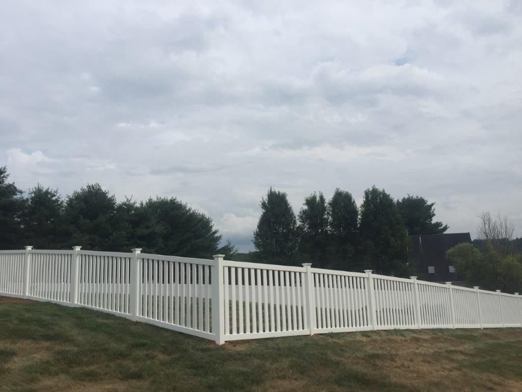 White fence along a grassy hill under a cloudy sky, with trees in the background.