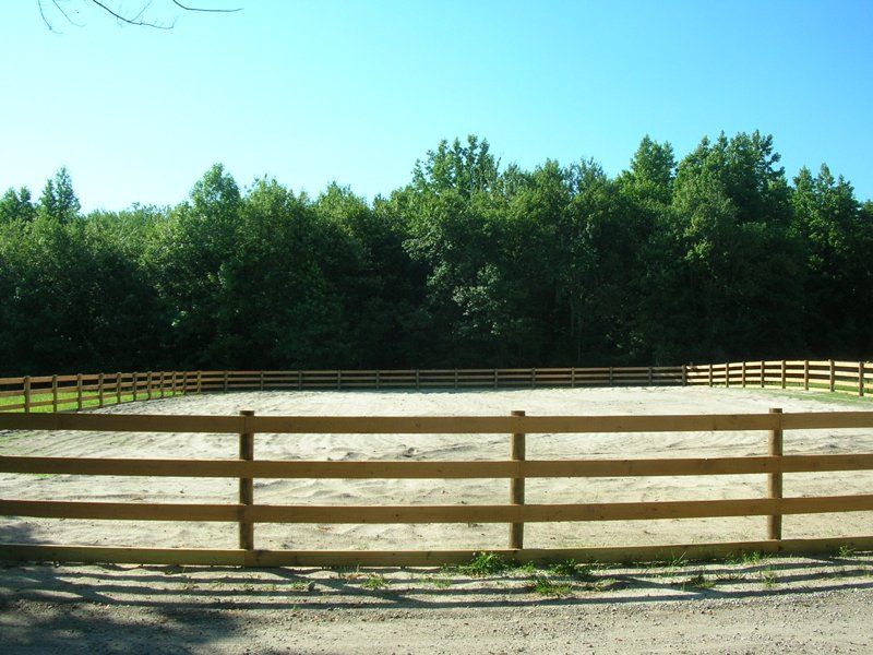 Wooden fenced corral with sandy ground and green trees under a clear blue sky