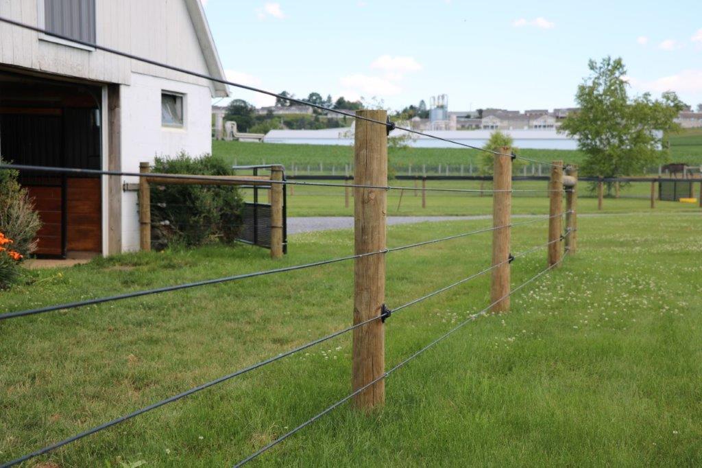 Wooden post-and-wire fence beside a white building in a grassy field with water in the distance