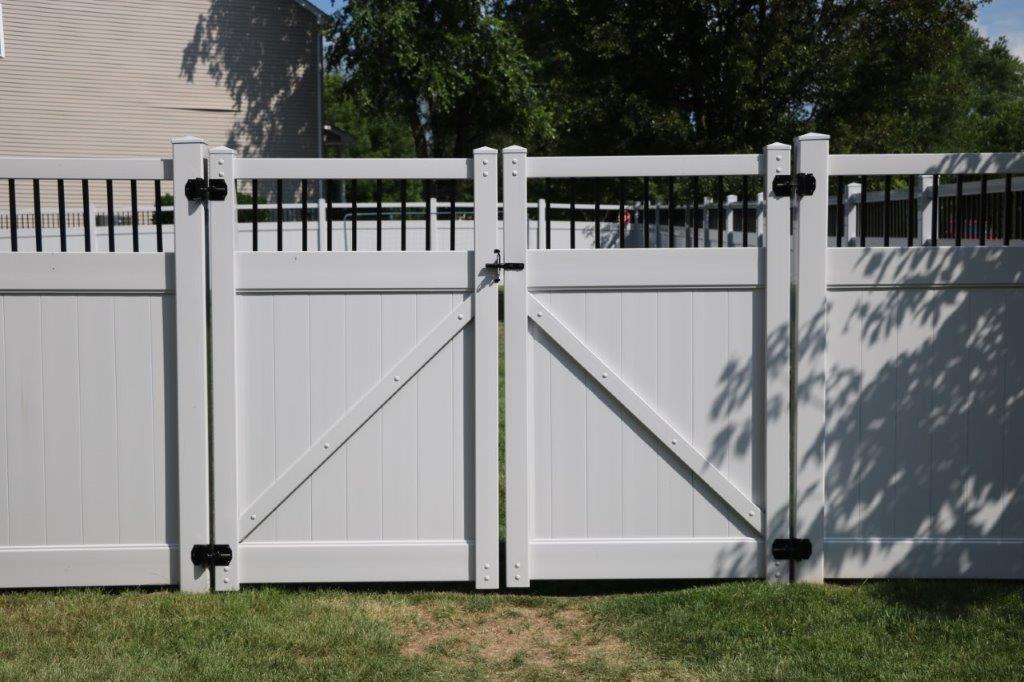 White wooden backyard gate with diagonal braces and black latches in front of a house and grass