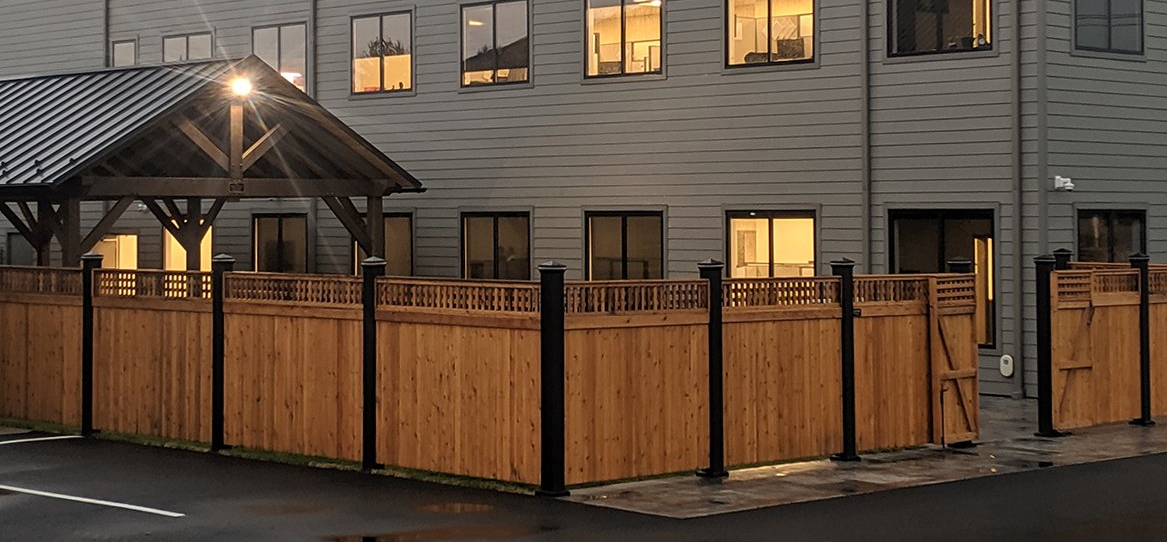 Wooden-fenced outdoor dining area beside a lit building at dusk