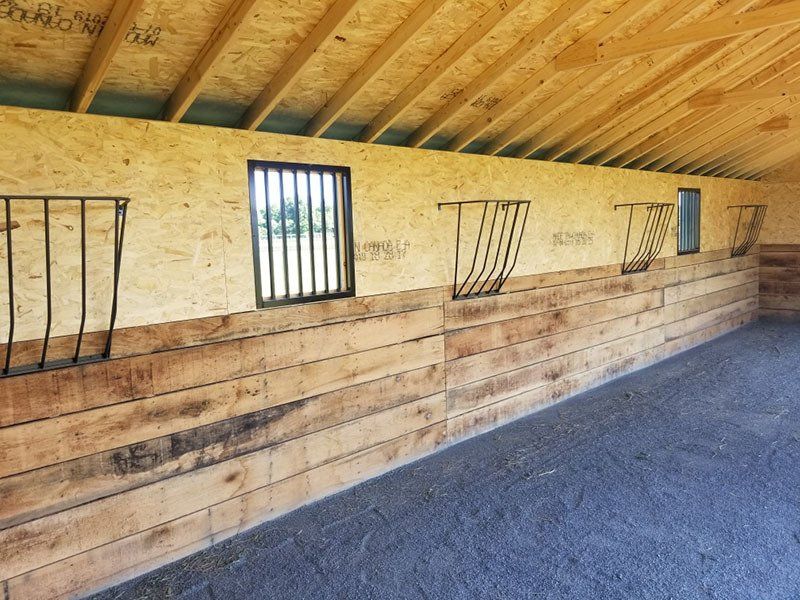 Long wooden horse stall wall with barred windows under a slanted roof inside a stable