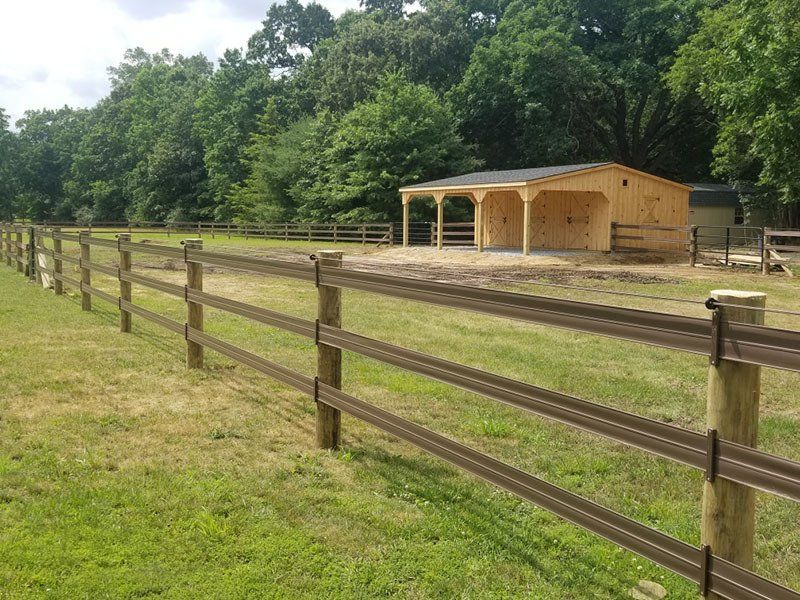 Wooden fenced paddock with a small tan shed beside a tree line on a grassy field.