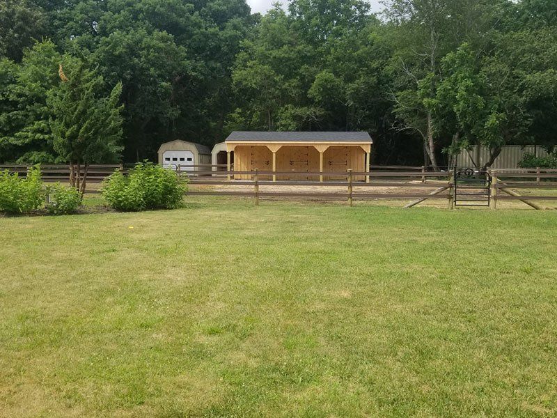 Wooden pavilion in a grassy park, with trees and a small fenced garden in the background