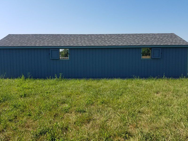 Blue barn-like building with a gray roof in a grassy field under a clear sky