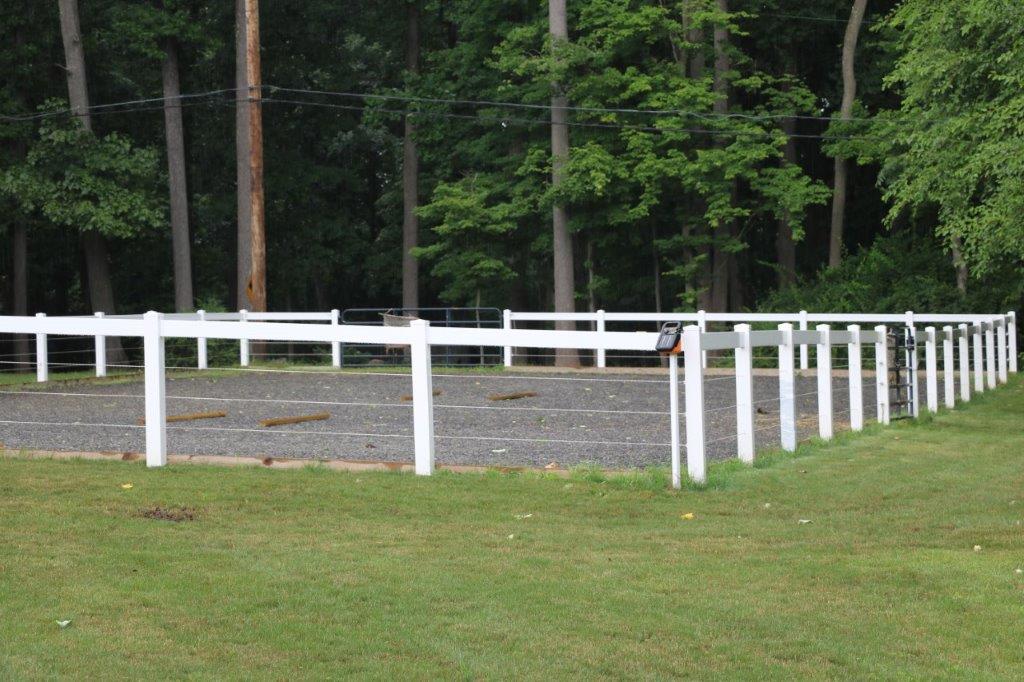 White fenced paddock in a grassy yard with trees in the background