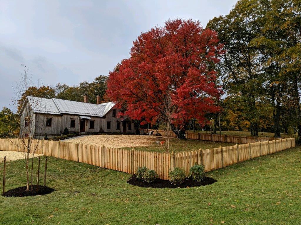 Old barn beside a fenced yard with a bright red autumn tree and grassy field