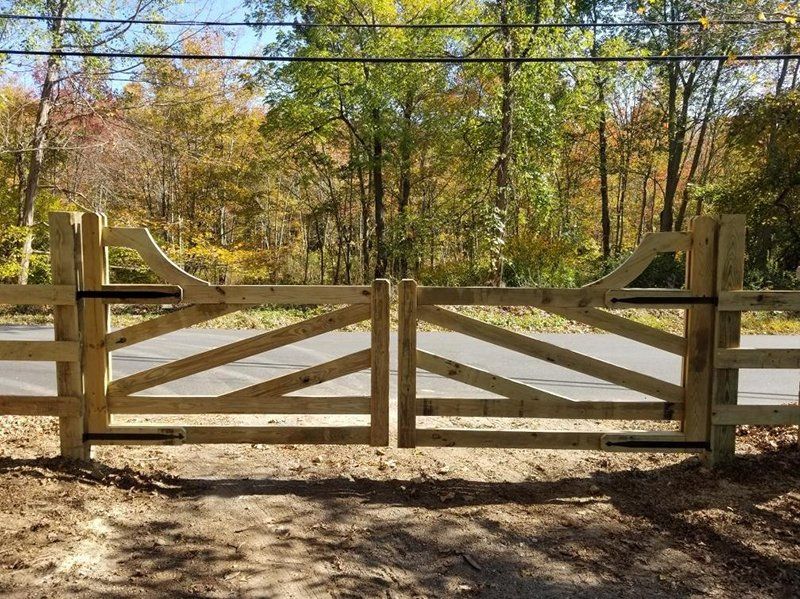 Wooden farm gate in front of a dirt path, with autumn trees in the background.