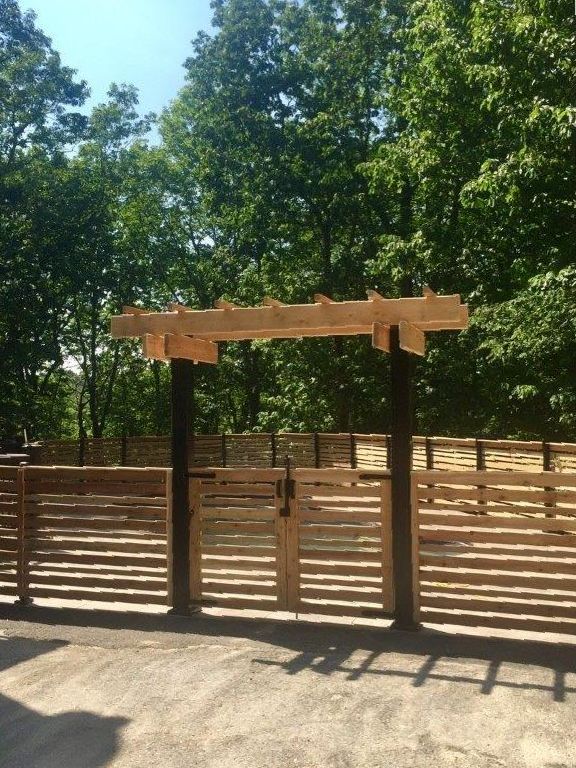 Wooden gate and fence at a wooded park entrance under bright sunlight