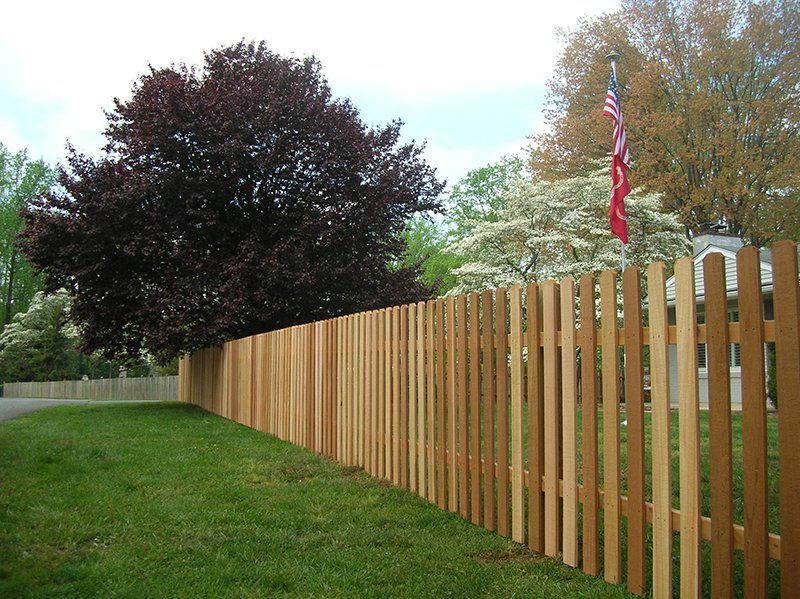 Wooden fence lining a grassy yard with trees and an American flag in the background