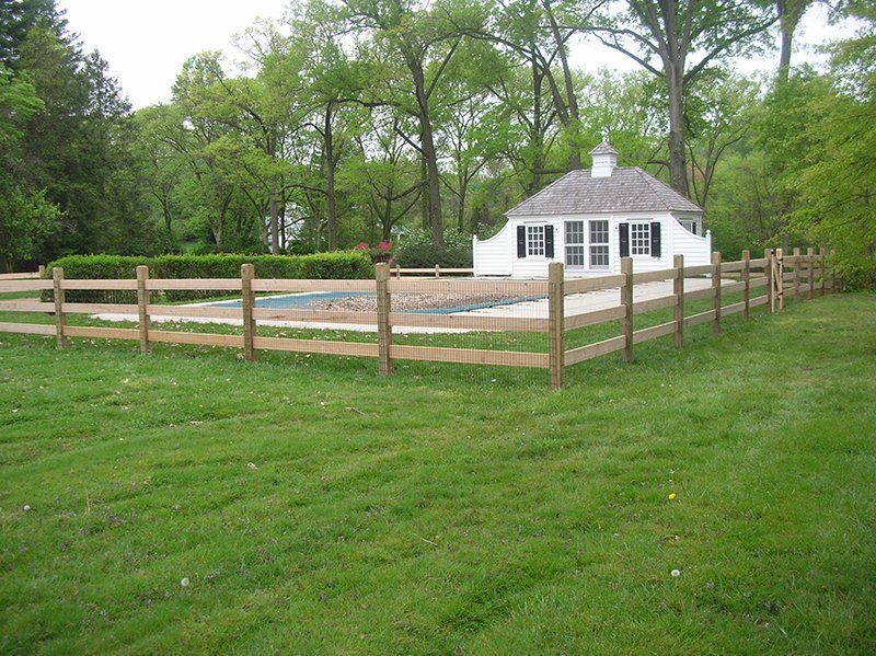 White gazebo beside fenced pool area in a grassy park, surrounded by trees.